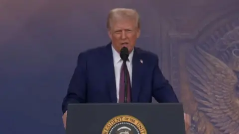 President Donald Trump speaks into a microphone.