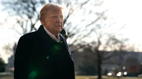 Donald Trump wears a dark coat and white shirt and speaks to members of the press as he and first lady Melania Trump prepare to depart the White House aboard Marine One on January 24, 2025 in Washington, DC