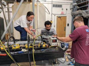 The researchers are crowded around the apparatus each busy with a different part.