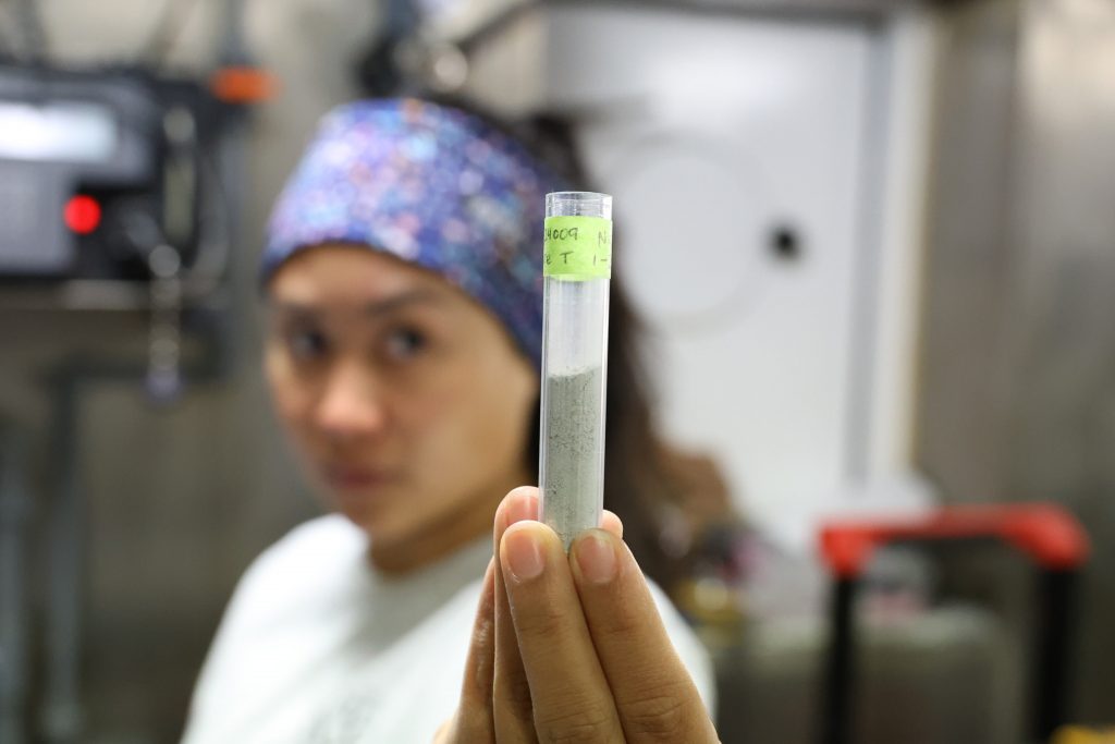 Close up of a scientist (Pascual) holding a plastic vial half full with grey powder.