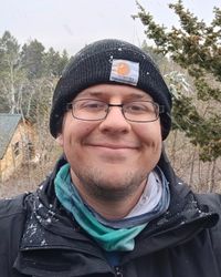 A selfie photo of Riley in front of a tree, wearing a beanie.