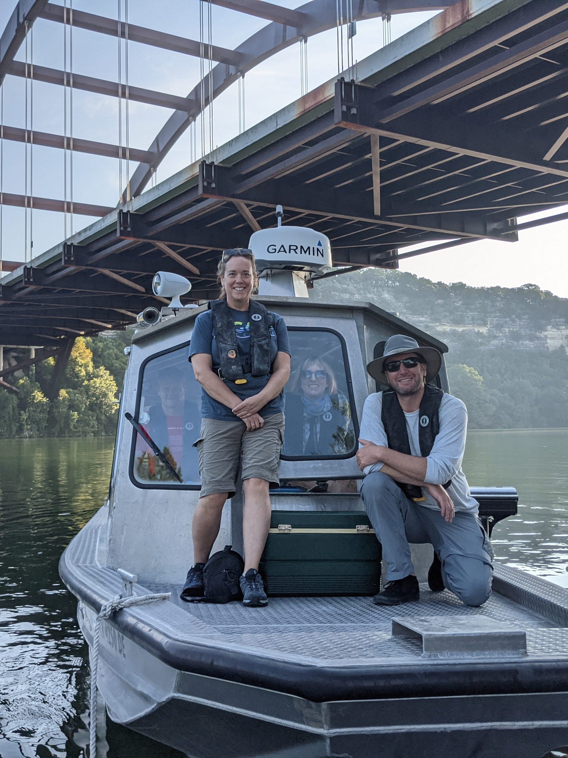 Photo of people standing on the deck and inside of a small boat under Pennybacker bridge