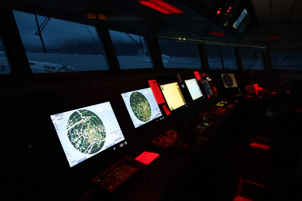 The darkened bridge by night. Screens glow under red lights.