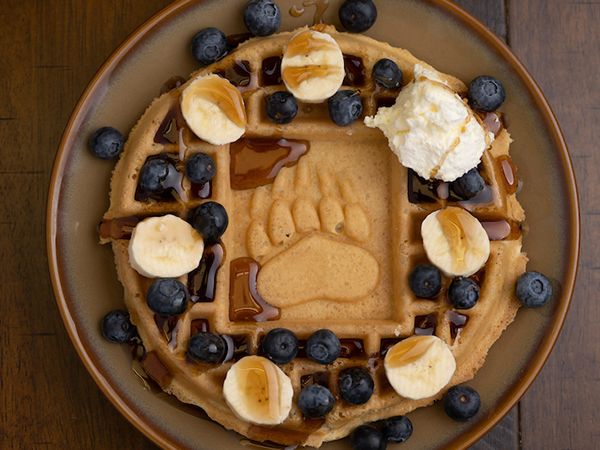 A waffle with "UM" baked in the middle is adorned with blueberries, butter and whipped cream