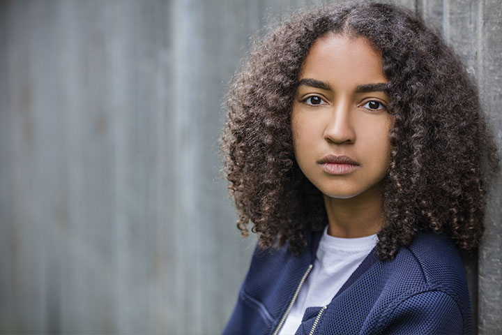 a brown skinned teen leaning against a fence