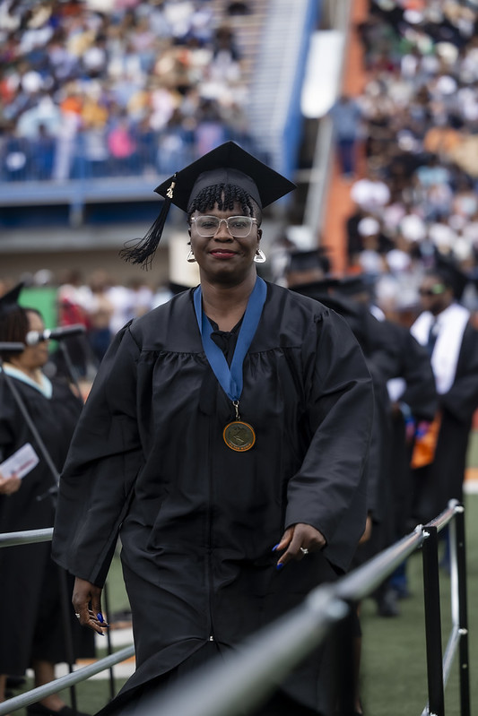 Woman in cap and gown walks across the stage at graduation