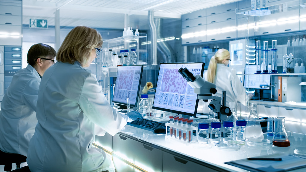 Scientists in laboratory looking at data and through microscopes