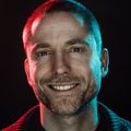 Aral Balkan portrait photo, facing the camera, studio quality lighting with red light and blue light on the sides against a black background