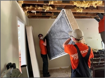 Two people in orange shirts move a bed during hurricane cleanup