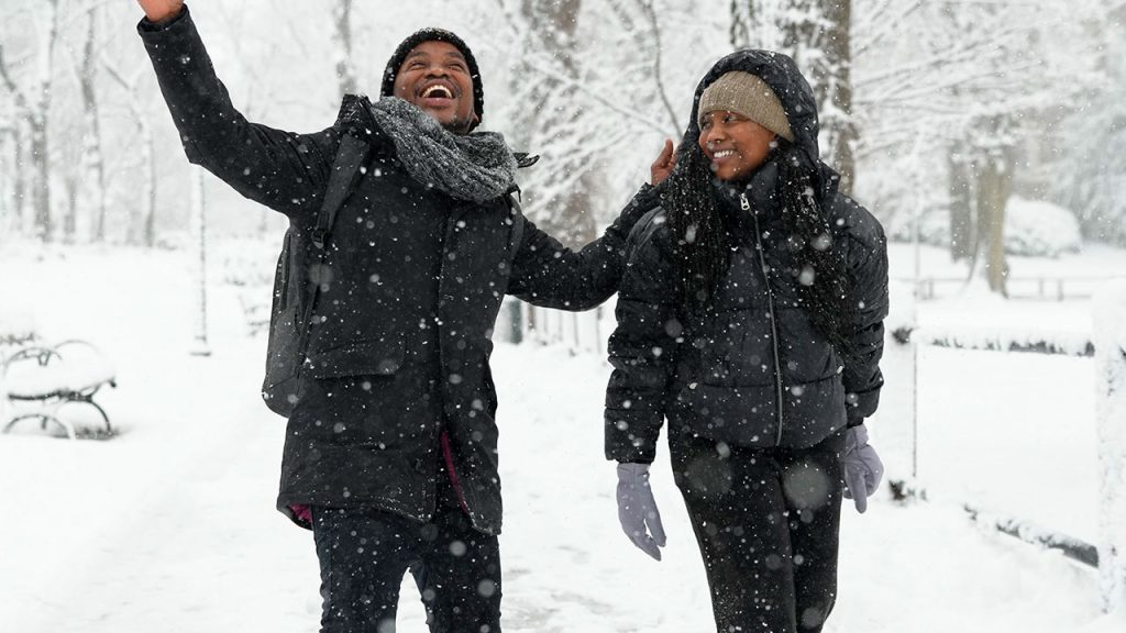 One male presenting student (left) and female presenting student (right) in jackets, enjoying the snow