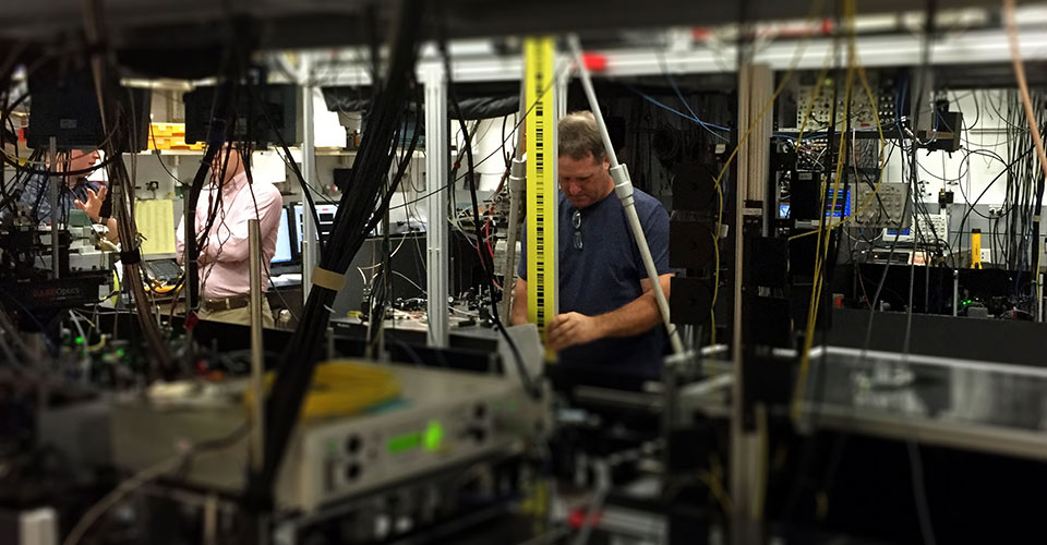 NOAA geodesist Steve Breidenbach holds a vertical leveling rod on top of a geodetic marker in the floor of a laboratory that contains an atomic clock at the National Institute of Standards and Technology in Boulder, Colorado. 