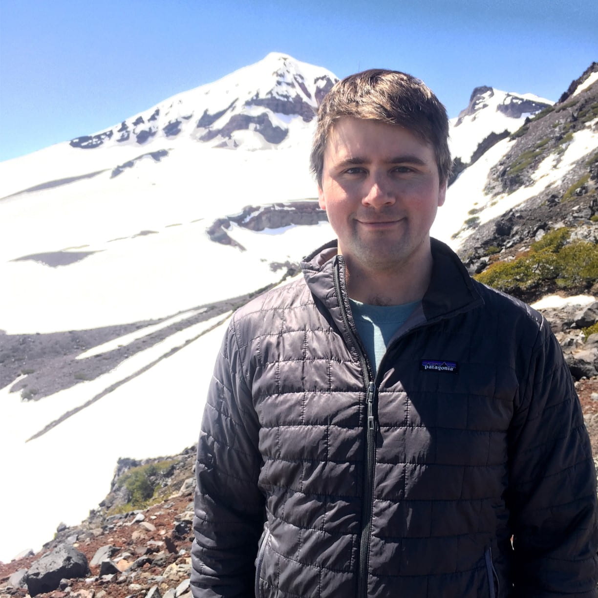 A man smiling for a photo near a glaciated mountain