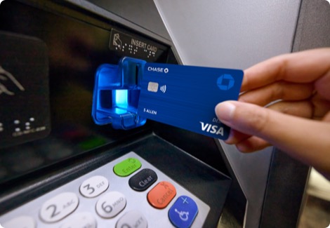 A hand inserts debit card into a Chase ATM machine to withdraw money