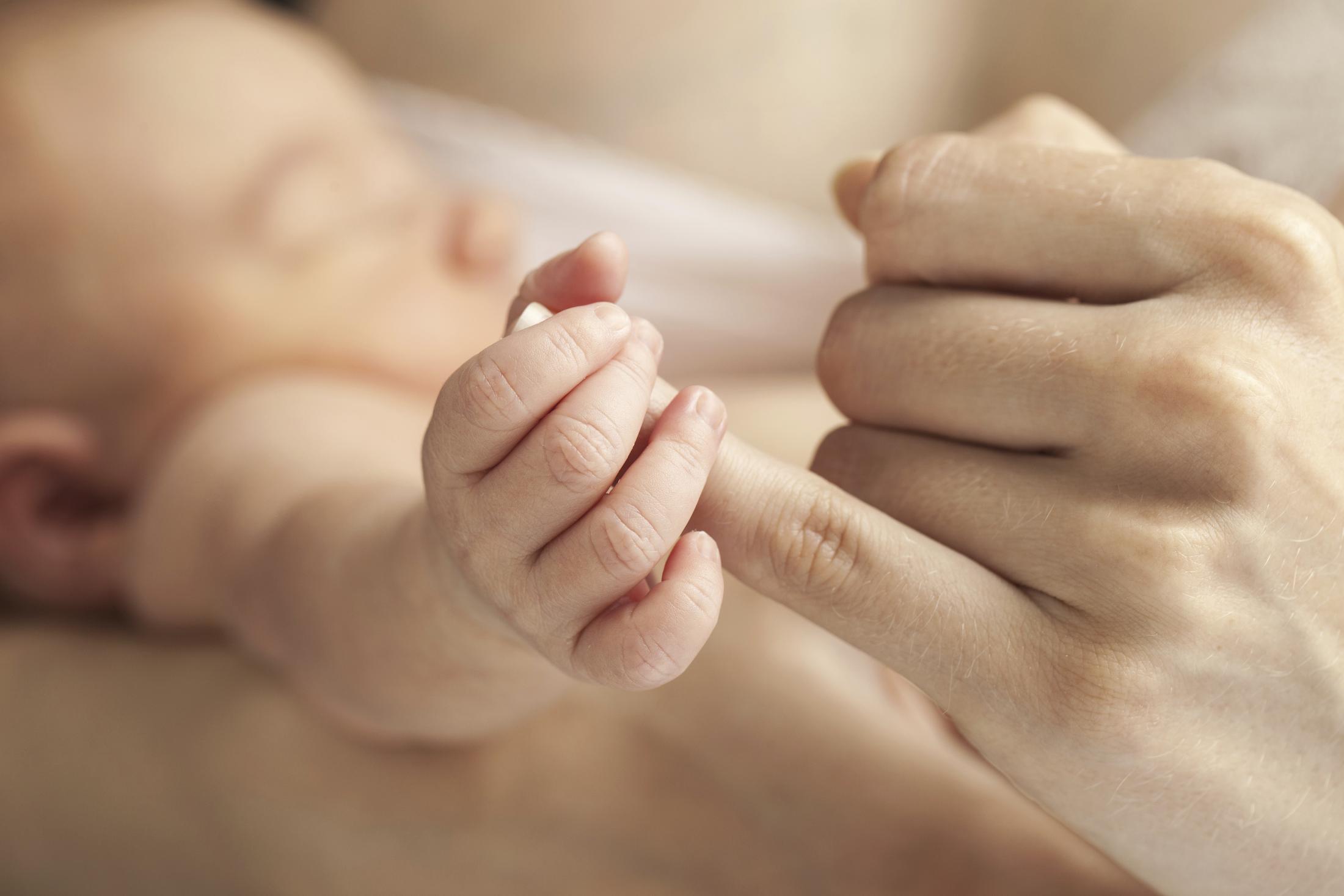 newborn baby holding pinky of adult caregiver