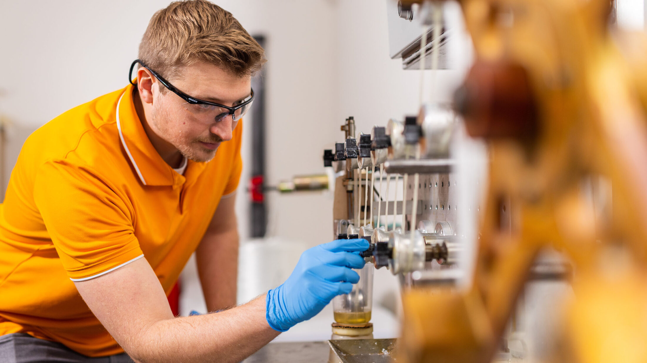 Willian Henken, in an orange polo shirt and safety glasses, turns a knob on the filament winder.