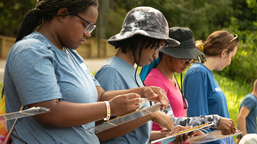 Three volunteers lined up holding clipboards and studying datasheets