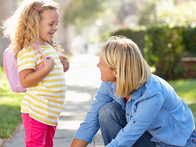 A parent tying their child's shoelace on the sidewalk.