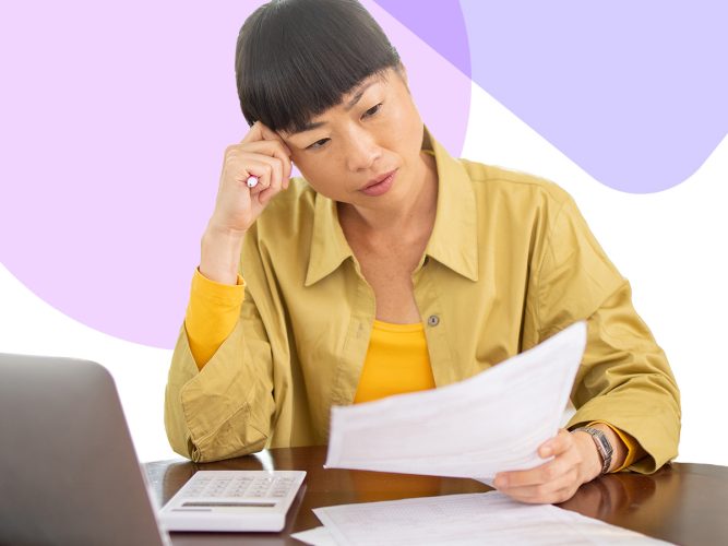 An adult examines a piece of paper while using a computer