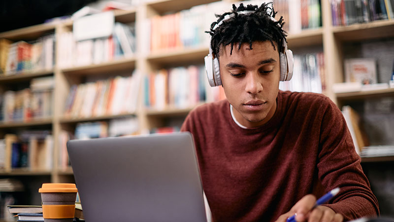 student wearing headphones and working on laptop in library