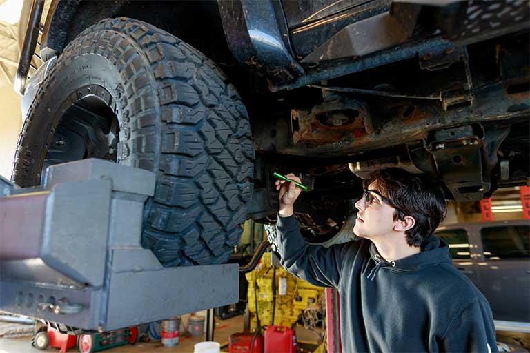 student looking at a car wheel while underneath it