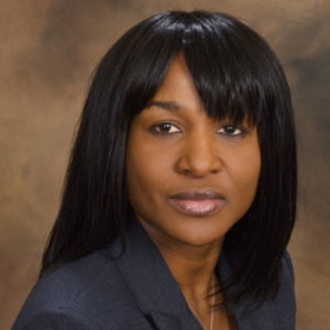 Woman with long dark hair and a dark gray suit, looking at the camera.