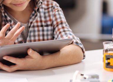 Smiling girl sitting in the science studio and using tablet while surfing the Internet