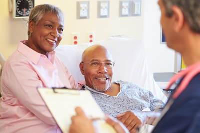 A man in the hospital talks with his doctor as his wife listens.