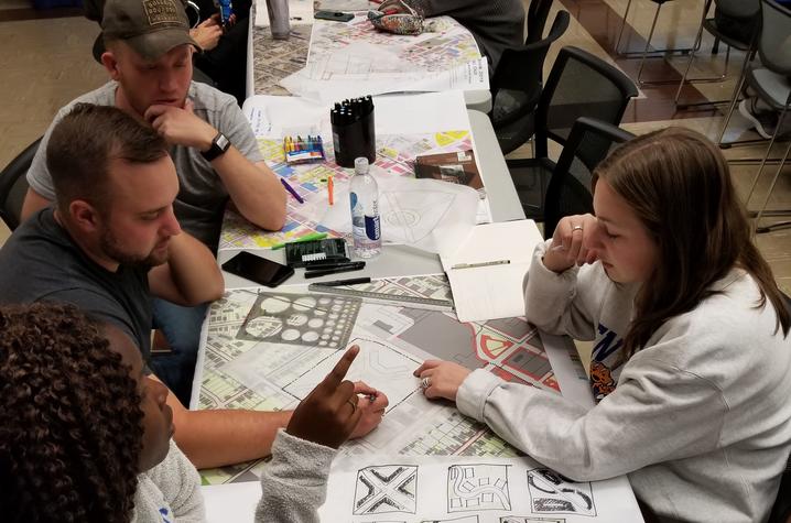 Four students sitting at table with sketches and designs