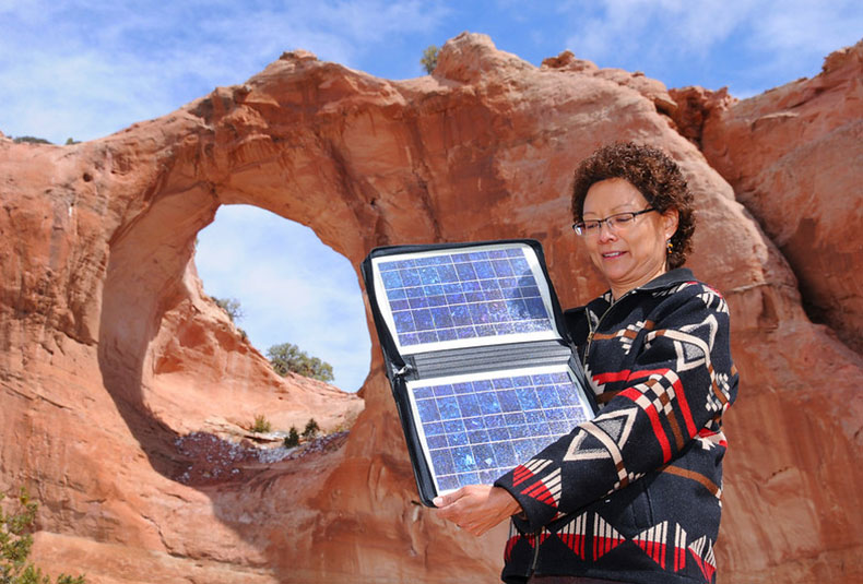 A Native American woman is pictured in front of Window Rock holding a book 