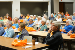 People in a crowded auditorium listen to a speaker at Fall in the Gardens