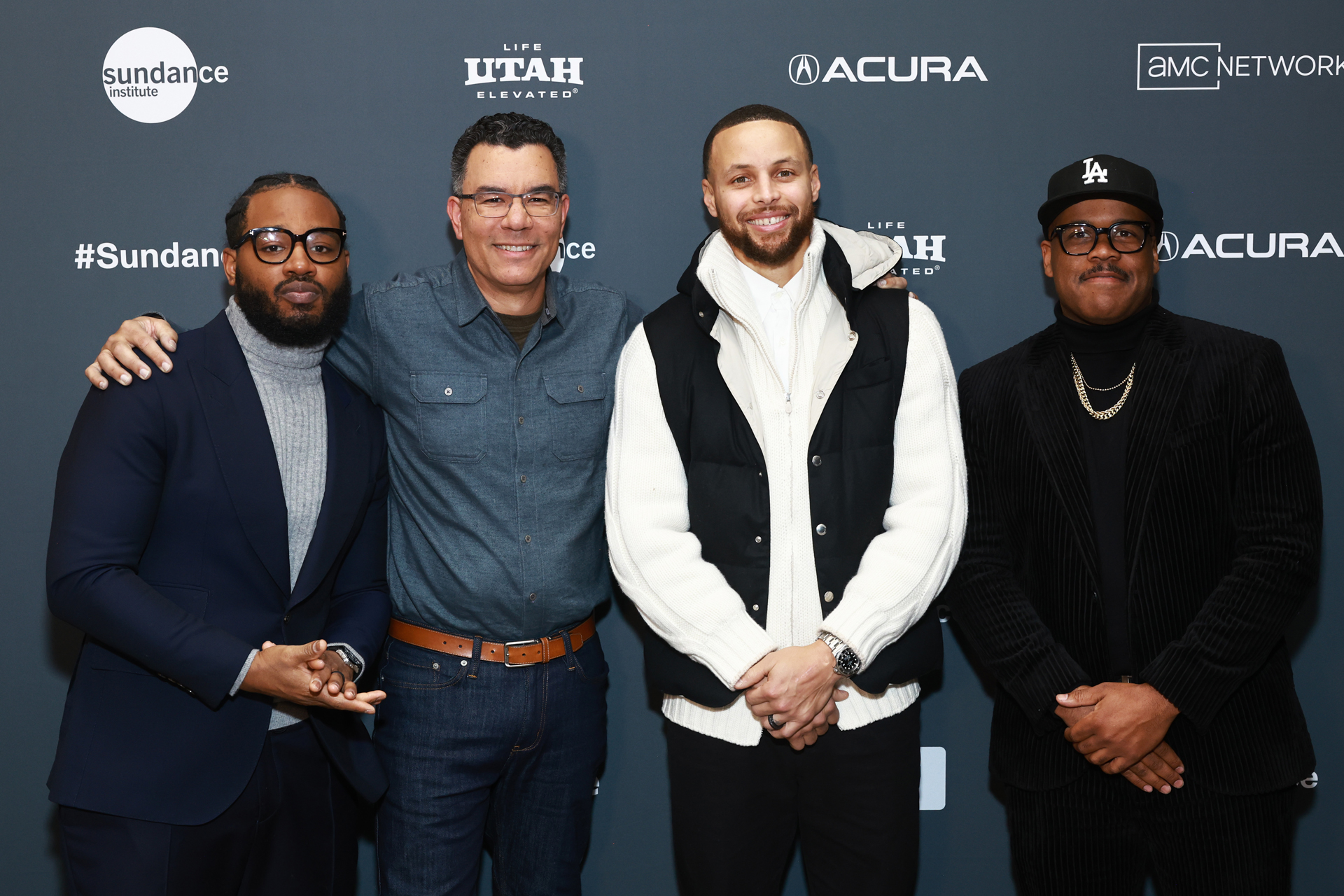 Four men stand smiling in front of Sunday step-and-repeat