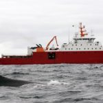 A research ship on the sea with a whale in the foreground