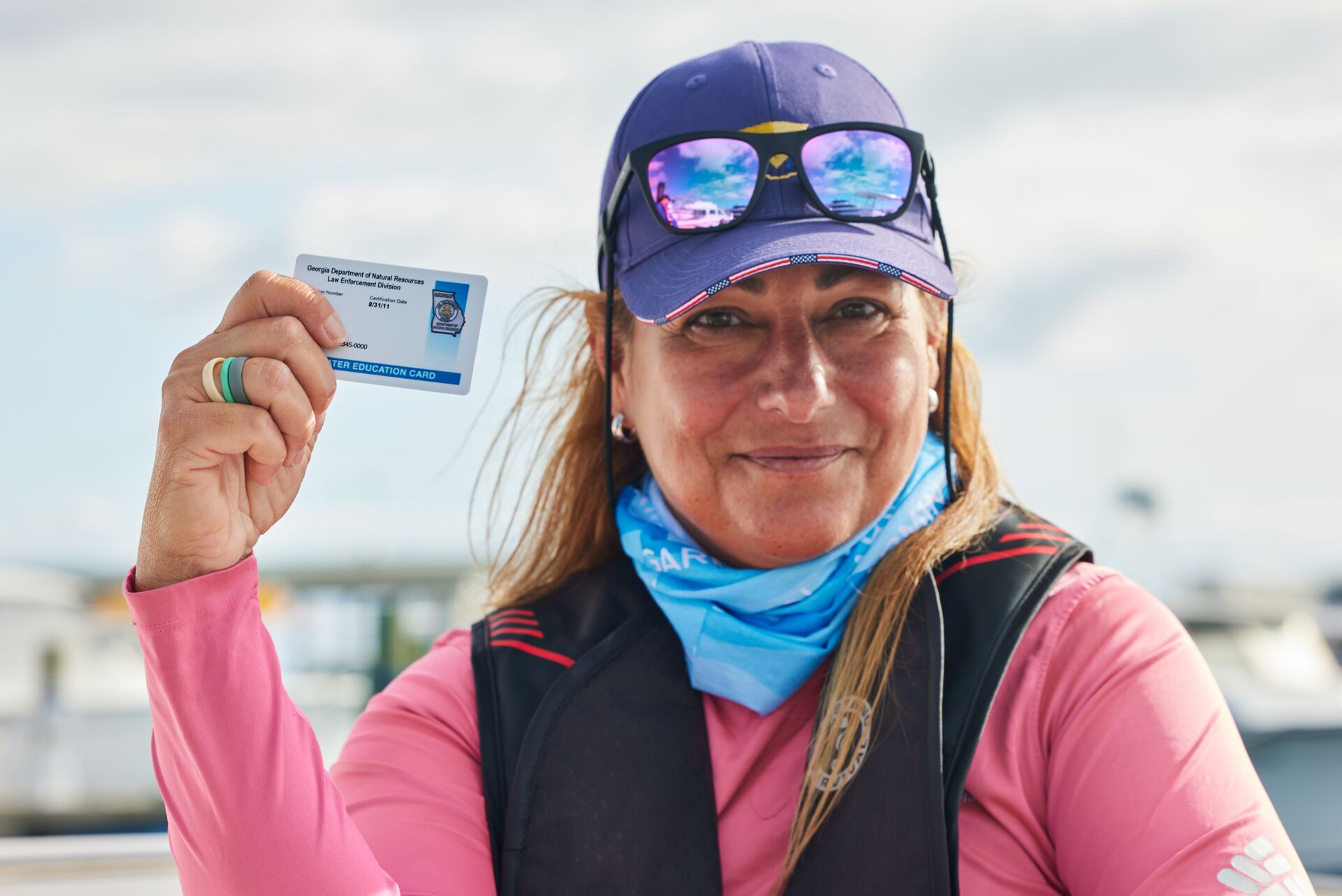 A woman holds up her boating license while on a boat. 