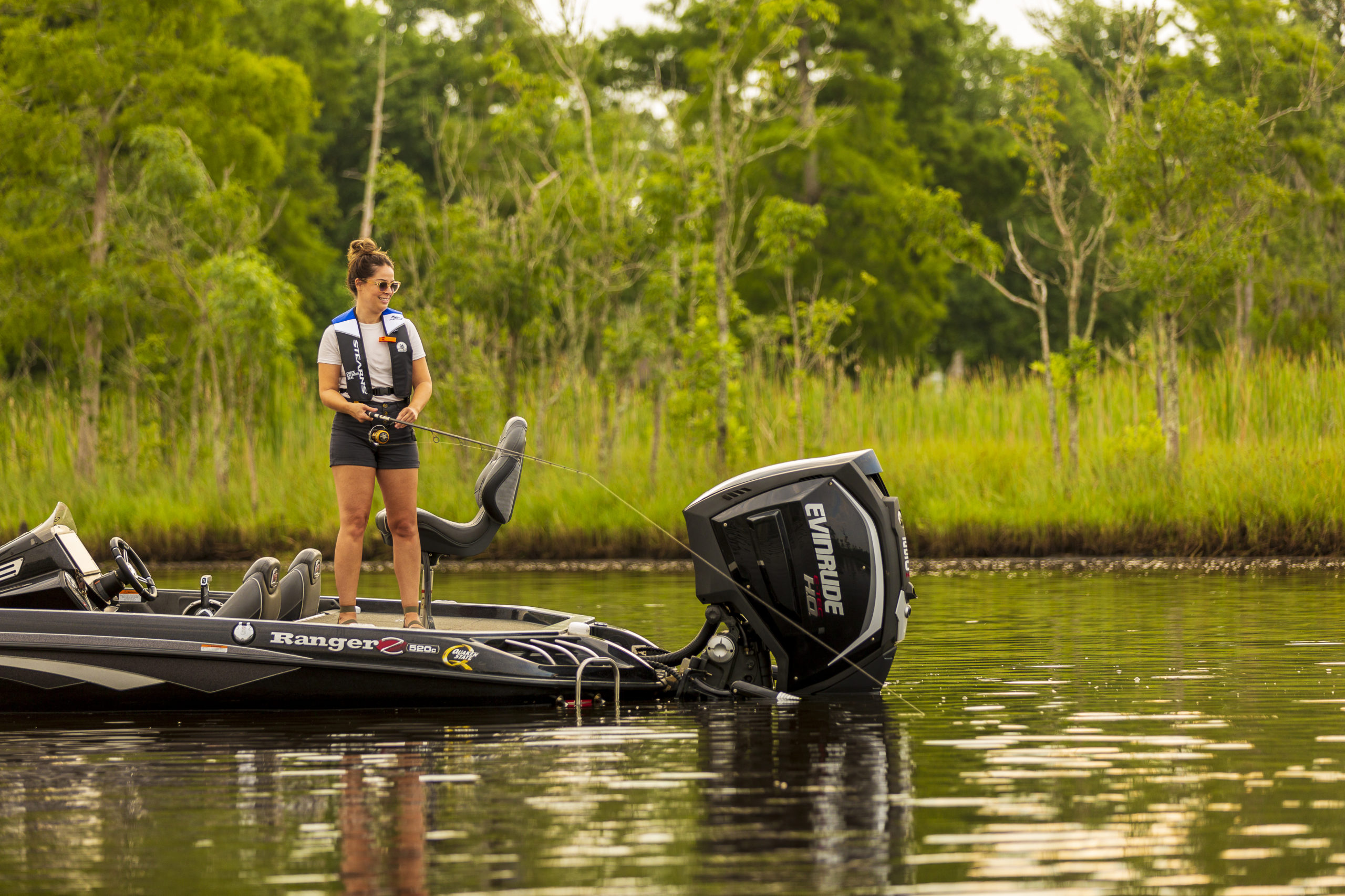 A woman wearing a lifejacket while fishing from a boat. 