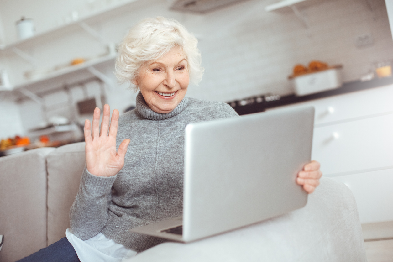 Happy senior woman waves to her laptop.