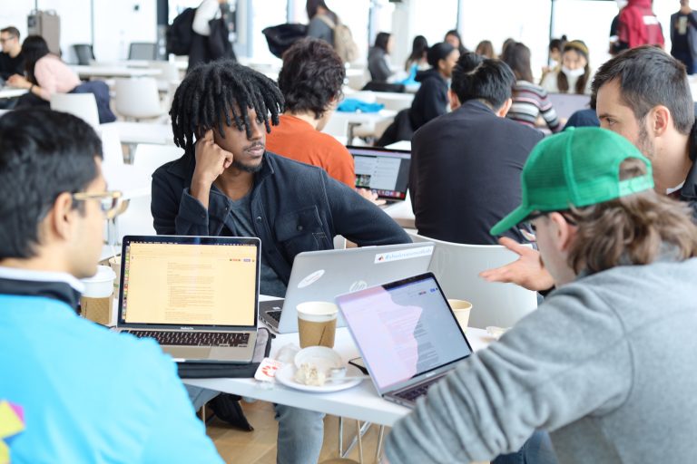 Photo of large group of students collaborating on laptops during a hackathon