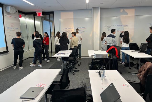 Photo: A group of college students in a modern classroom with shared tables and chairs with wheels on the bottom.