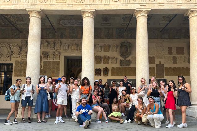 Photo: A group of college students stand in front of a building in italy with classic italian columns and stone architecture