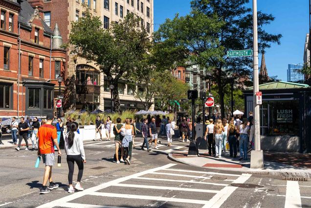 Photo: Small groups of people walk down an urban street lined with red brick brownstones and iron fences