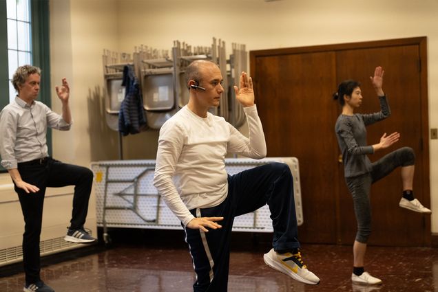 Photo: A man wearing headphones and casual workout attire guides a tai chi class with about 5-6 people following his movement