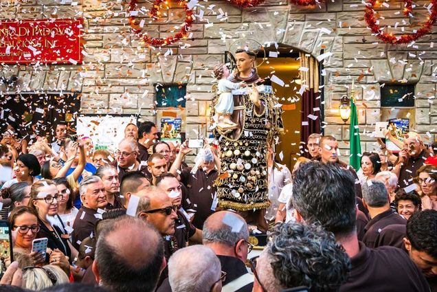 Photo: A picture of a procession where many people are gathered around a statue of Saint Anthony with confetti flying around