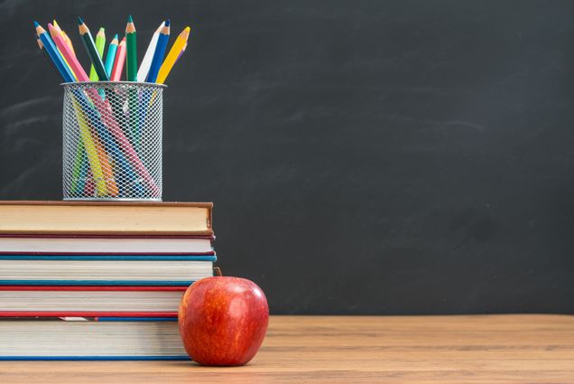 Photo: A desk in front of a chalkboard with a stack of book's, pencils in a cup, and an apple on top