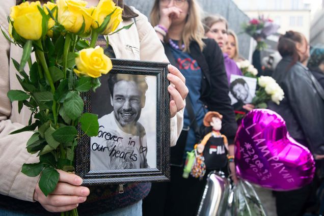 Photo: A memorial for former One Direction star Liam Payne. A woman is holding yellow roses and a black and white framed photo of Liam Payne that says "forever in our hearts"