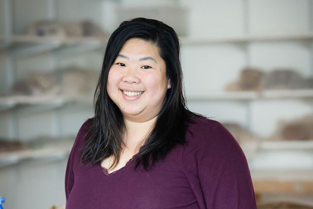 Photo: Kim Wong poses for a portrait photo in her pottery studio in a purple shirt.