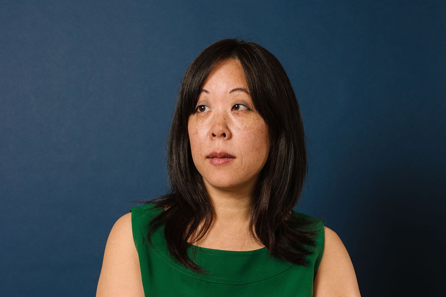 Photo: An Asian woman with mid-length dark hair in a green tank top posing in front of a dark background and looking off to the side