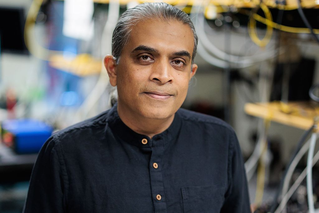 Photo: A man in a dark blue half-button down long-sleeve standing in a lab with his hands in his pockets