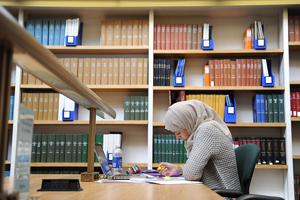 Legal history and jurisprudence at BU Law. Woman studying at BU Law Library in front of bookshelf.