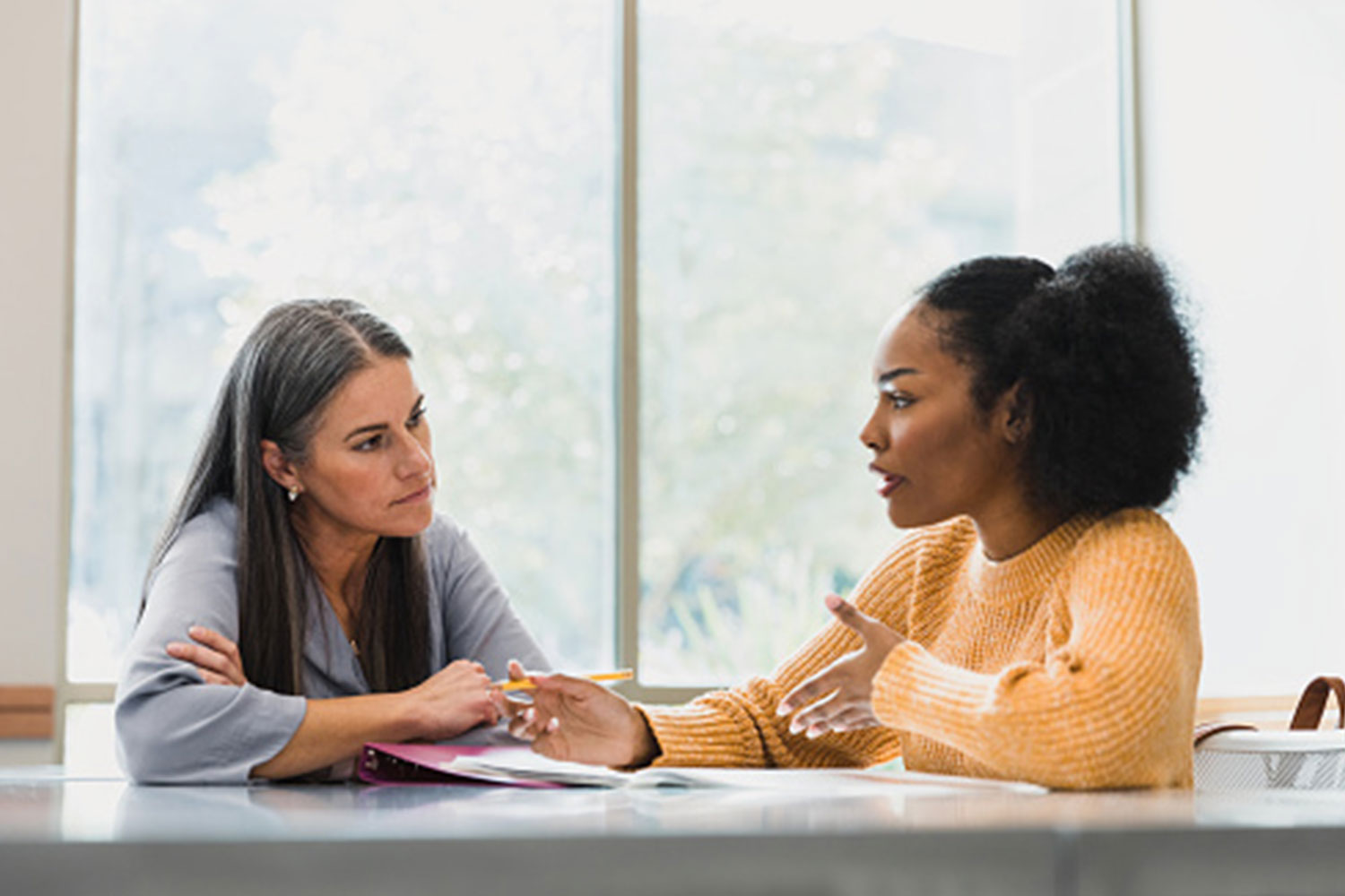 African American female student speaking with seasoned female at table