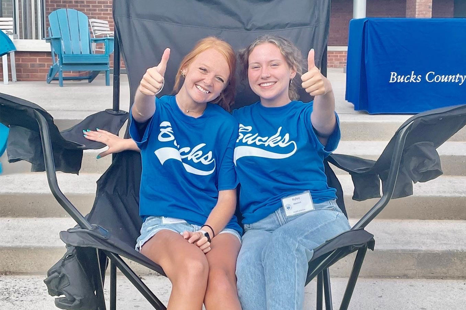 Two female students sitting side-by-side giving a thumbs-up