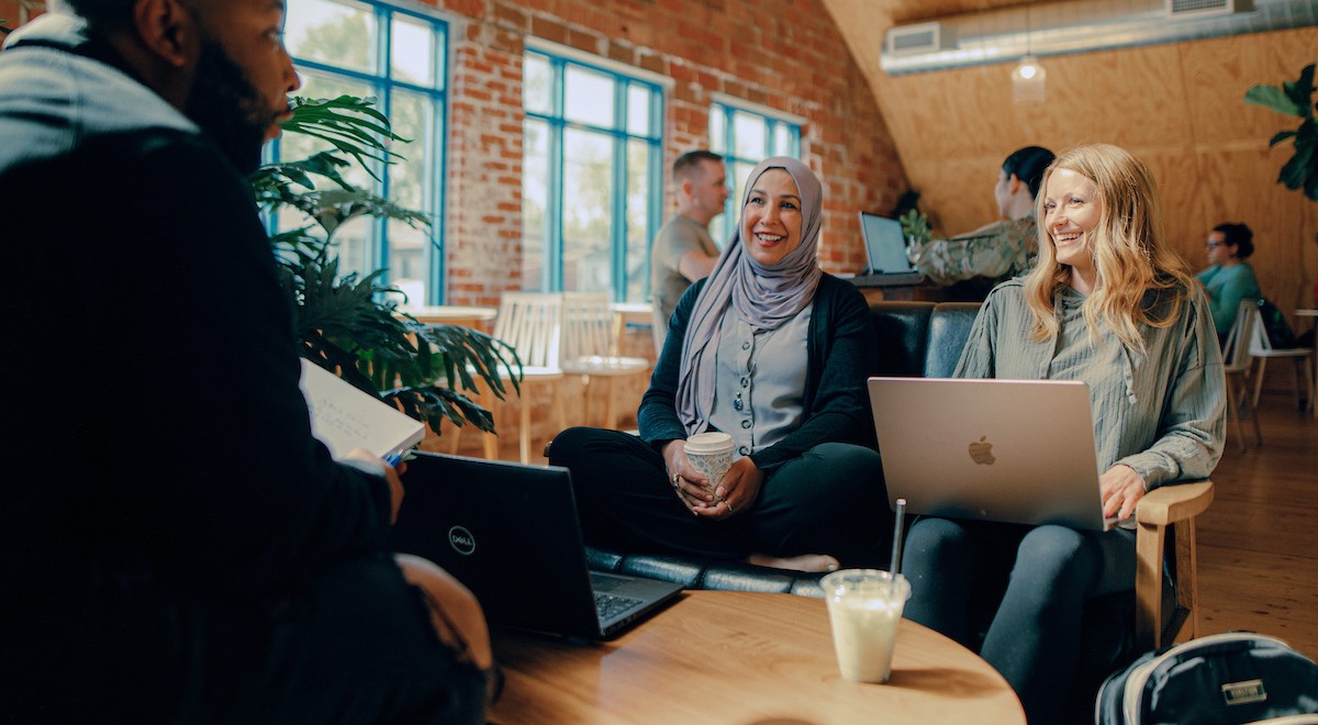 Three students sitting around a table, having a discussion, while using laptops.